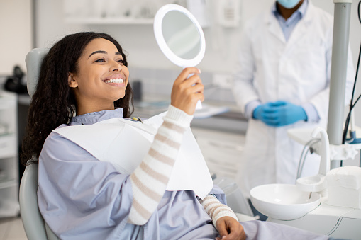 Dental Patient Looking At Mirror After Dental Treatment In Clinic